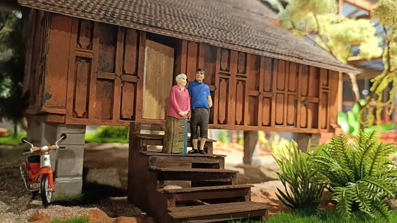 Handcrafted miniature wooden Malaysian home with two tiny people on its steps